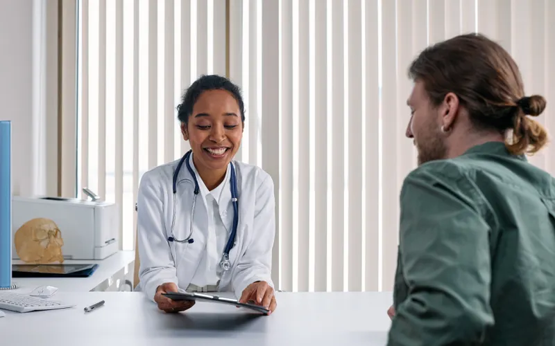 A doctor smiles while talking with a patient across a desk